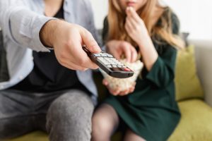 Man holding remote and eating popcorn with woman